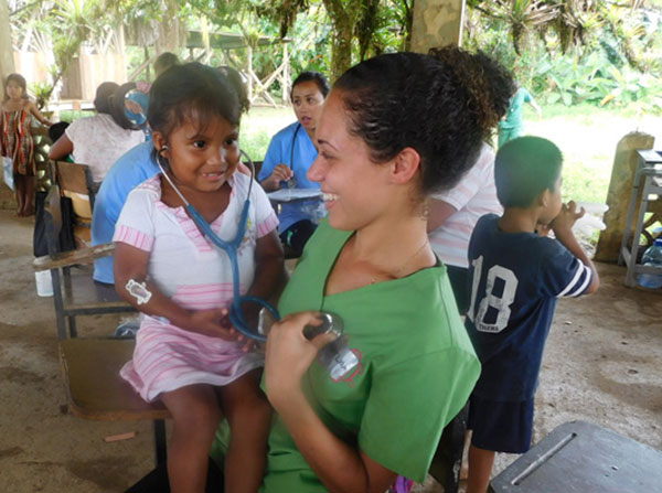 USC master’s in global medicine student Kaylha Munn exchanges provider roles with her young patient, sharing her stethoscope during clinic down time.