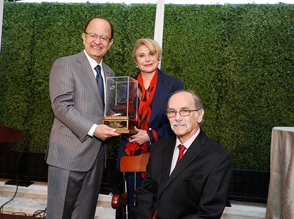 USC President C. L. Max Nikias, left, hands a miniature chair to Ghada Irani during the installation celebration honoring Arthur Toga, seated, as the inaugural holder of the Ghada Irani Chair for Neuroscience, held Nov. 17 on the Health Sciences Campus.