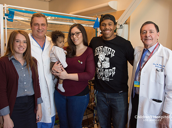 Baby Donovan Daniels and his parents post-transplant in 2016, joined by doctors and, at left, Lydia Hand, now 18.