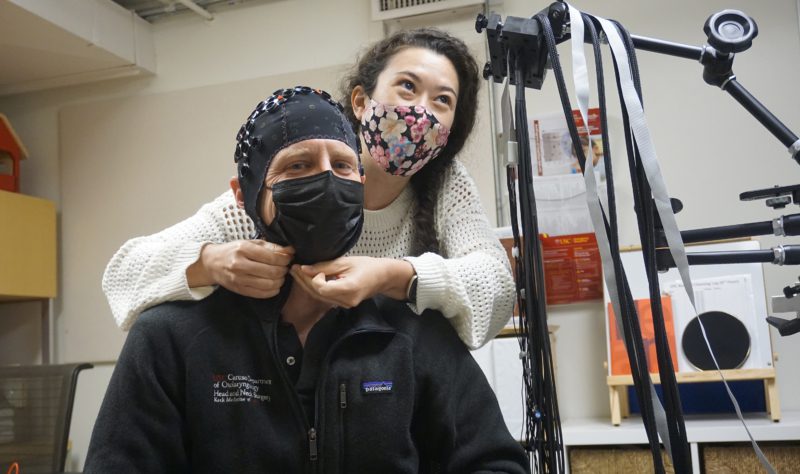 Photo of a researcher securing a device on Dr. Goldsworthy's head in an experiment.