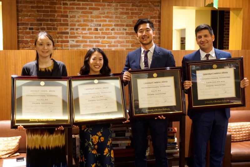 Four doctors standing in a row, holding diplomas.