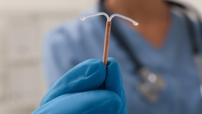 Doctor holding T-shaped intrauterine birth control device on blurred background, closeup