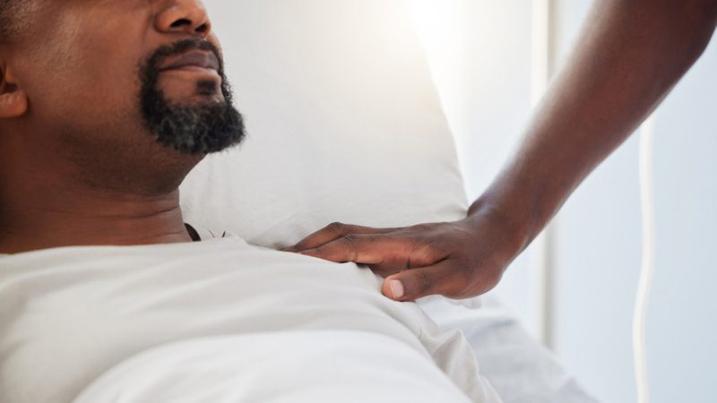 Sick, ICU or ill man lying on a hospital bed with support and care from a person inside. Closeup of an African American male patient getting medical treatment or aid for an emergency or cancer