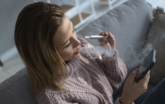 Leisure at home. Relax on the sofa, smoking electronic cigarette and browsing the social media.